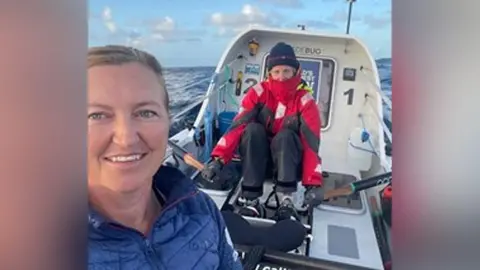 Emma Wolstenholme and a crew member on board their small rowing boat. She is in blue while her colleague wears a red overcoat and beanie hat