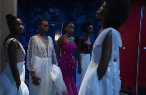 Getty Images Models waiting backstage wearing dresses.