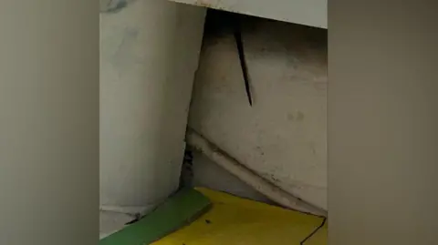 A mice's tail hanging from underneath a gap in the bathroom of a flat inside Meredith Court, Hulme, and mice droppings on a yellow mat