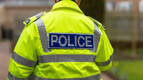 A policeman walking away from the camera on a residential street, which is out of focus.