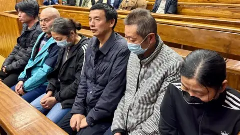Buthanani Thobela/Department of labour Six of seven people sentenced for human trafficking sit in a courtroom, some of them in masks