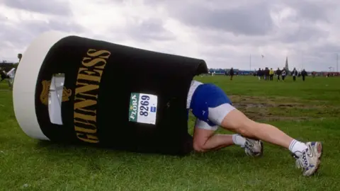 Getty Images A fun runner puts on his 'pint of Guinness' costume for the 1998 London Marathon
