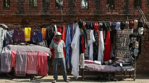 Getty Images A vendor selling clothes, caps and other accessories waits for customers at his roadside stall on a hot summer day in Varanasi on April 18, 2026.