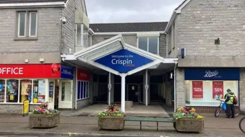 A closed shopping centre entrance with a sign reading welcome to the Crispin Centre