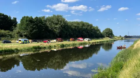 Shaun Whitmore/BBC A rescue boat on Middle Level Main Drain with emergency services on the bank