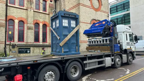Zion Baptist Church A Tardis is on the back of a flat-bed truck parked at the side of a large brick church.