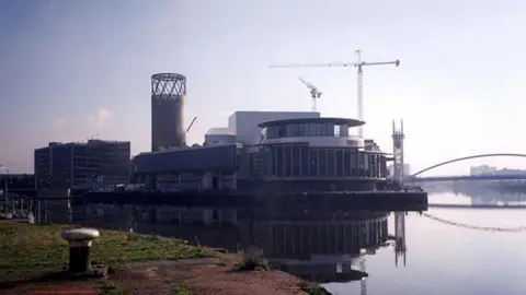 External view of The Lowry theatre on Salford Quays. There is a crane in the background and a bridge.