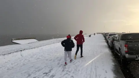 Walkers on the beach at Aberdeen making their way through heavy snow