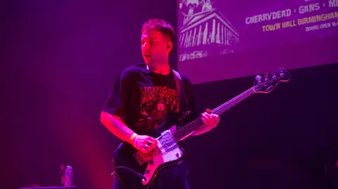 A man in a black T-shirt playing a bass guitar