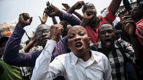 Getty Images Supporters of the former candidate of the Lamuka opposition coalition, Martin Fayulu, shout in protest after the protest march organized on June 30, 2019, the Independence Day, in Kinshasa was stopped by the police. - Police in the DR Congo capital Kinshasa used teargas on June 30 to break up an opposition march and blocked a car transporting former presidential candidate Martin Fayulu.