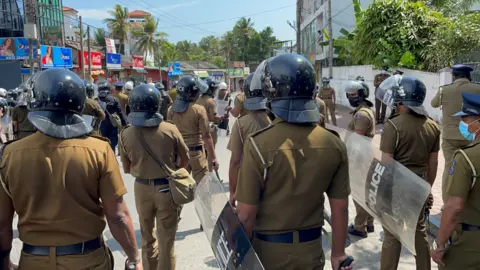 Police in riot gear form rows facing protesters