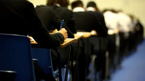 Pupils in black school jumpers taking exams in an exam hall.