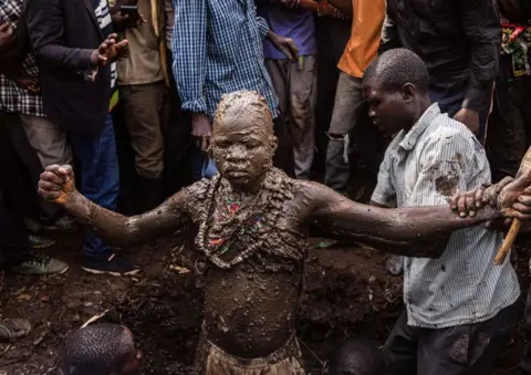 AFP A boy covered in mud with his arms stretched out wide.