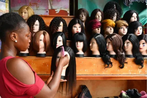 AFP A woman combs and cares for synthetic wigs on a stand.