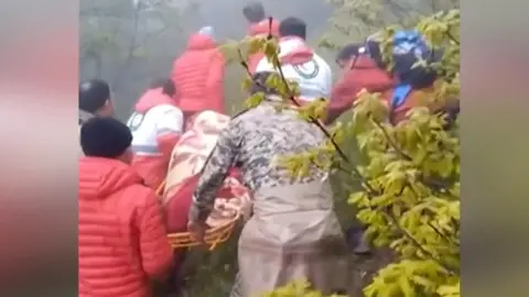 Rescue team carries a body wrapped in cloth on a stretcher