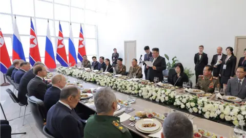 KCNA Kim Jong Un delivers a speech at a banquet table with the Russian president and officials