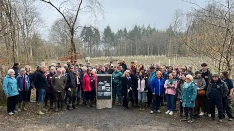Dozens of people standing around the new plinth at Stover Country Park with freshly-planted trees in the background.