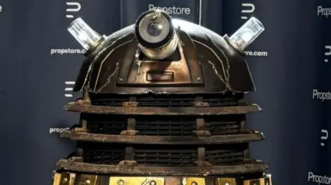 A close up of a battle-damaged Dalek with Propstore branding behind it