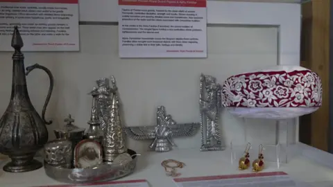 A museum exhibit of items including silverware that are heirlooms of the Zoroastrian religion on a table.