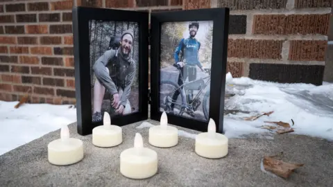 Two framed images show Alex Pretti sitting crouched over by the camera in a wood, and the other holding a bicycle while wearing a helmet and cycling gear, with LED candles placed in front of the frames on the doorstep to Alex Pretti's house in Minneapolis, taken on 26 January.
