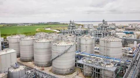 Vivergo/ PA Media The exterior of the Vivergo Fuels plant, with huge metal cannisters at the front, metal railings and other grey metal buildings behind. A wide river estuary can be seen in the background, alongside fields and countryside.