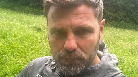 A man with short light brown hair and a short light brown-grey beard looking at the camera.