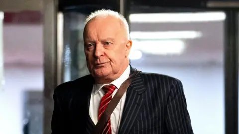 PA Media Phil Shiner outside Southwark Crown Court in London. He wears a pinstripe suit and red tie.