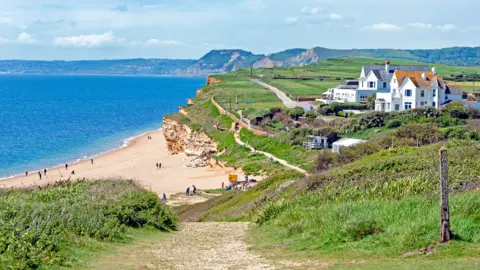 Getty Images A view of a beach and cliff landscape on a sunny day. There are buildings on the cliff edge to the left.