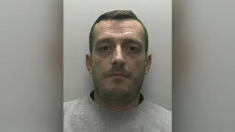 Hampshire Police Gareth Roberts mugshot. He has short brown hair, brown stubble and is wearing a grey sweatshirt.