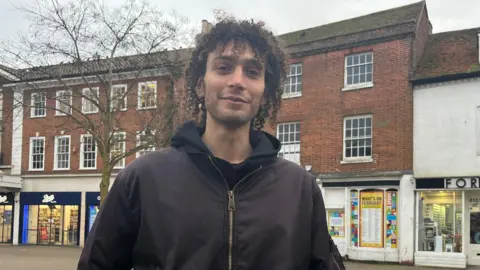 Julia Gregory/BBC Nadeem Badran being voxed in Epsom, Surrey. Nadeem is wearing a black hoodie and jacket, and has almost shoulder length hair. 