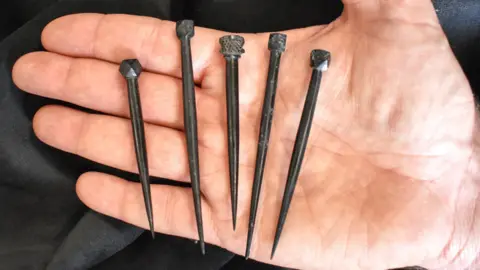 Colchester Archaeological Trust Five black hairpins laid out in the palm of someone's hand.