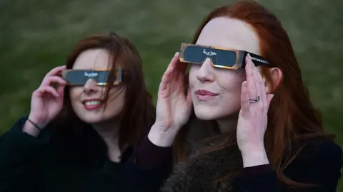 Getty Two women look at a partial solar eclipse through protective glasses over Stonehenge in Wiltshire, south west England on March 20, 2015. 