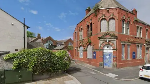 Google The Queen's Arms in Barrow, a red-brick building with boarded up doors and windows.