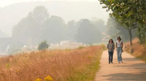 Two people walking along a path. The sky is hazy