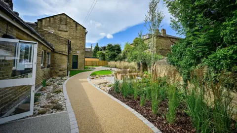 Bradford Council A path down side of a building with plants on the right side of it