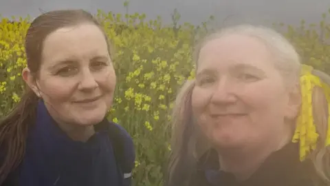 Two woman taking a selfie with yellow flowers behind them