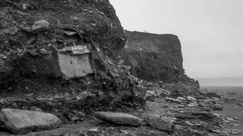 Colin Pickett A black and white shot of a cliff with items falling from it 