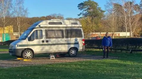 Rachael Meller wearing a blue jacket and brown trousers standing next to a small campervan at the site in Woodhall Spa.