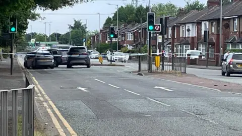 Image shows a police cordon in place on a main road, with tape surrounding several vehicles. 