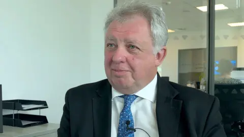 A headshot style picture of David Sidwick, Dorset's police and crime commissioner. He is wearing a black blazer, blue tie and white shirt.