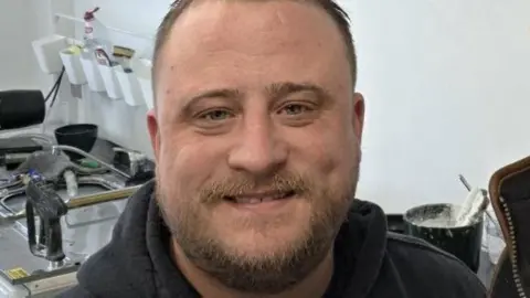 A close up of a selfie of Martin Roberts stood next to someone else who is out of shot. He is stood in front of a collection of medical equipment.