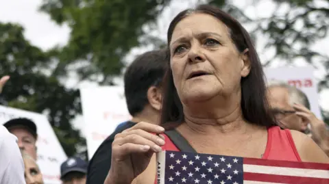 A female protester who supports Donald Trump's refugee plan in South Africa holding an American flag.