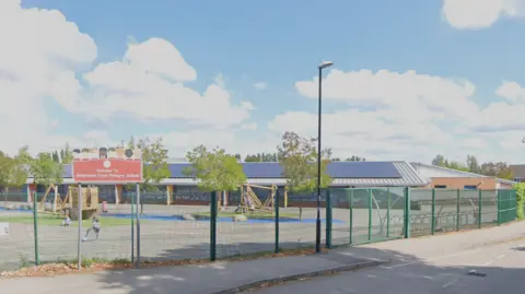 Google An animated image of Aldermoor Farm Primary School, which includes a playground surrounded by a green metal fence. A road and pavement run alongside.