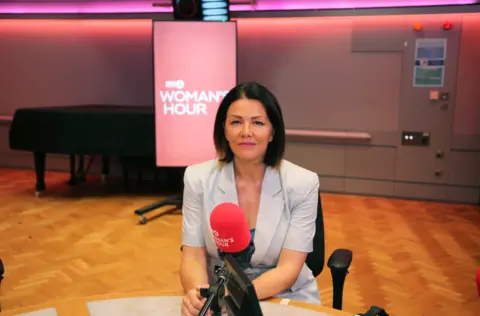 A woman with dark, bobbed hair sits in front of a microphone