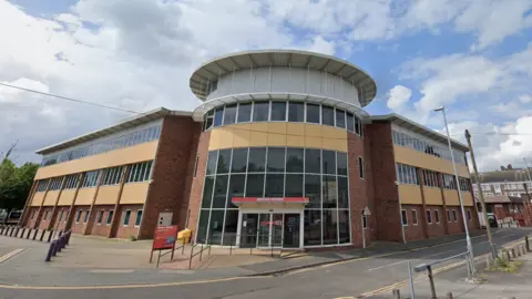 A three-storey office building with a rotunda at one corner and panels of yellow cladding between the floors.