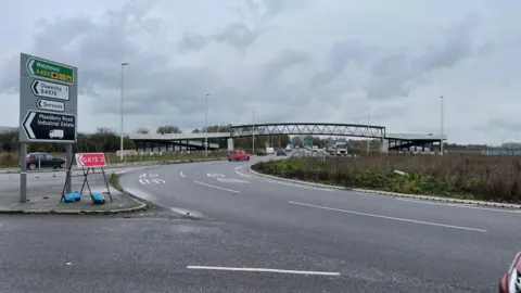 The Mile End roundabout near Oswestry with cars, bushes and road signs in the background.