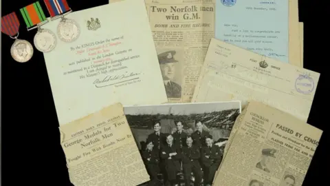 Noonans Mayfair A collection of newspaper clippings, black-and-white photographs and three medals belonging to Samuel Thompson. The items have been laid on a black background.