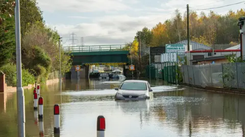 A road is overwhelmed by floodwater in Rotherham, abandoned cars are seen near a bridge
