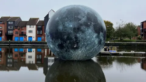 The giant Luke Jerram artwork Fallen Moon in Bridgwater Docks. Behind it flats on the waterside are visible