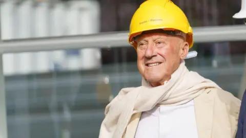 Getty Images Lord Norman Foster wears a yellow hard hat, a white shirt and a cream jacket and scarf